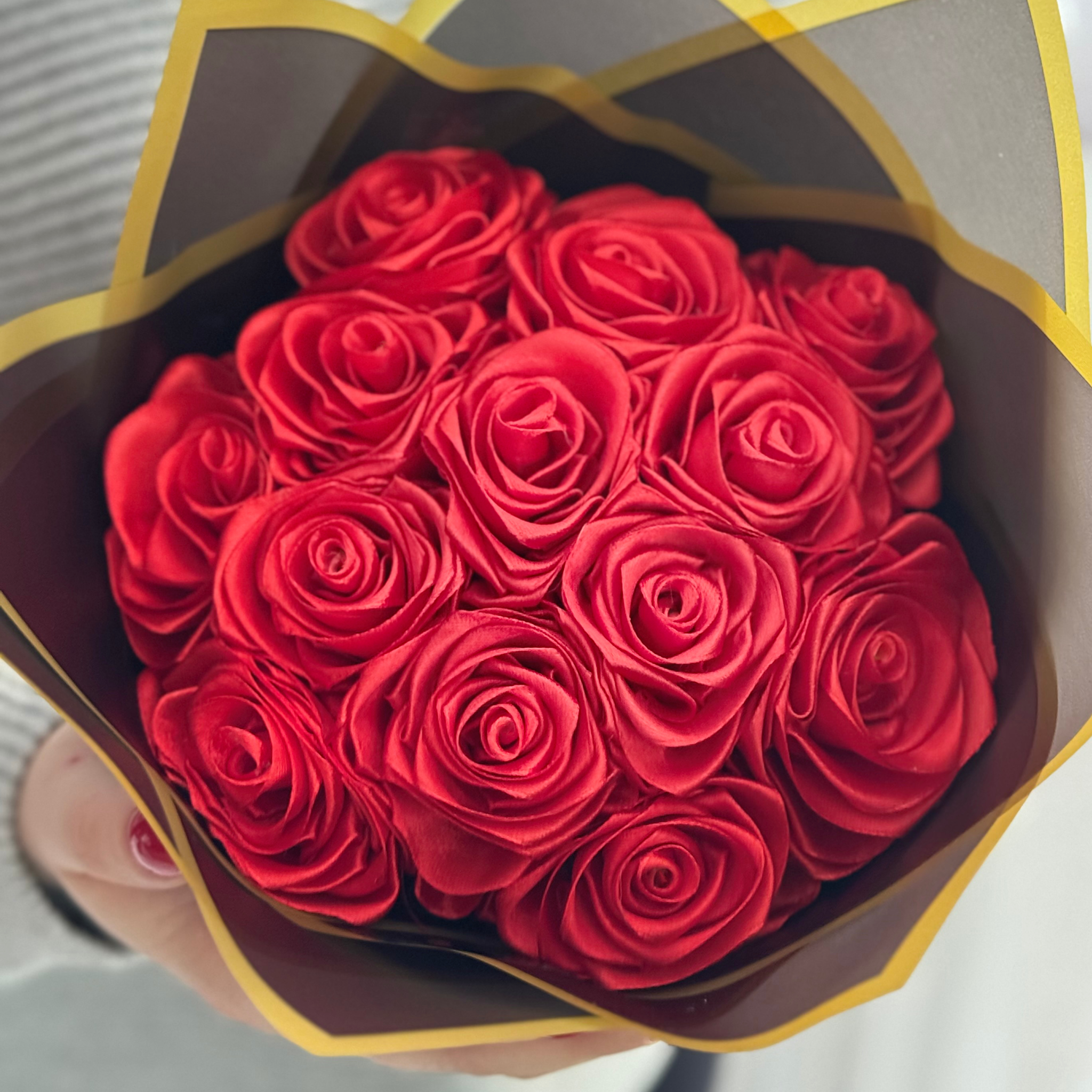 Osoba na zdjęciu trzyma pięknie udekorowany wieczny bukiet z trzynastu róż. Bukiet zawinięty jest w czarny aksamitny papier.